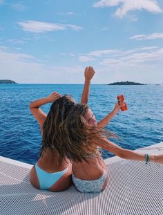 two women in bikinis sitting on the deck of a boat with their arms up