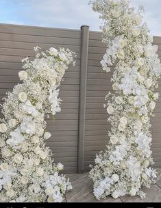 two tall white flowers are on display in front of a wall with a fence behind them