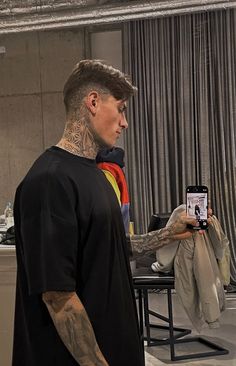 a man with tattoos is looking at his cell phone while standing in front of a chair