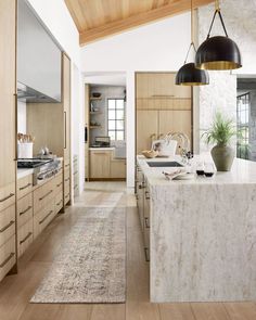 a large kitchen with an island in the middle and wooden cabinets on both sides, along with two pendant lights hanging from the ceiling