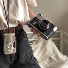 a person is holding a camera in their left hand while sitting on a bed with a white sheet