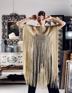 a woman wearing a gold fringed dress and black leggings standing in front of a mirror