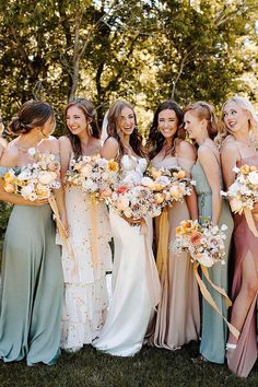 a group of women standing next to each other wearing dresses and holding bouquets in their hands