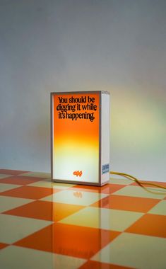 an orange and white box sitting on top of a checkered floor with the words, you should be digging it while its happening