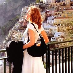 a woman standing on a balcony looking at the city from behind her with a black purse