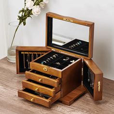 an open wooden jewelry box sitting on top of a table next to a vase with flowers