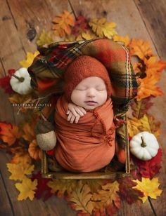 a newborn baby wrapped in an orange blanket laying on top of fall leaves