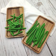 two wooden trays filled with green beans on top of a white wood table next to each other