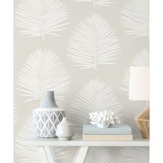 a white table topped with books next to a lamp and wallpaper covered in palm leaves