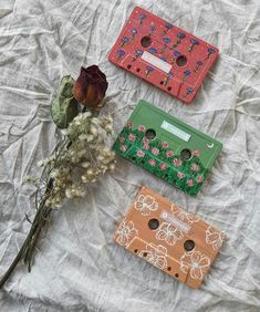 three different colored wallets sitting on top of a bed next to a dried flower