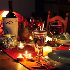 a dinner table with candles and wine glasses on it, surrounded by other plates and place settings