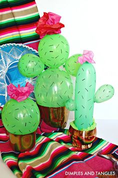 some green balloons are in the shape of cacti on a colorful table cloth