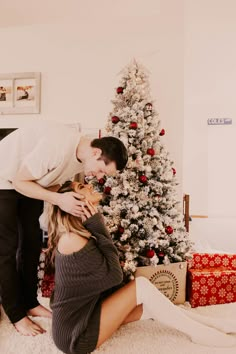 a man and woman kissing in front of a christmas tree with presents on the floor