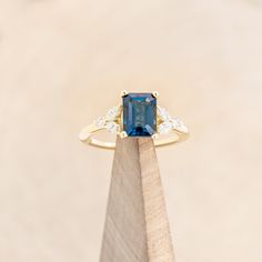 an engagement ring with a blue stone surrounded by white diamonds on top of a wooden stand