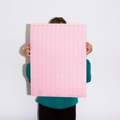 a woman holding up a pink piece of paper that has been cut out into squares