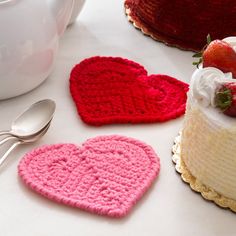 two crocheted hearts are next to a cake with strawberries on the top