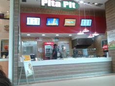 the inside of a pizzeria with people standing in front of it and menus hanging from the ceiling