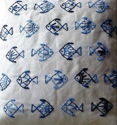 an embroidered pillow with blue and black fish on white fabric, sitting on a table