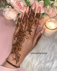 a woman's hand with henna on it next to flowers and a candle