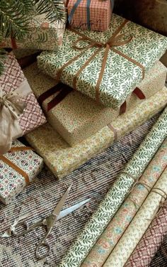 many wrapped presents sitting on top of each other next to a christmas tree and scissors