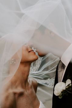 the bride and groom are looking at each other with veil blowing in the wind over their heads