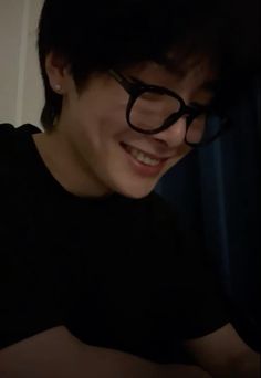 a young man wearing glasses and smiling at the camera with his eyes half covered in dark eyeglasses