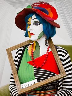 a woman with blue hair wearing a clown mask and holding a framed photo in her hands