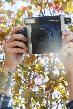 a person holding up a camera in front of a tree