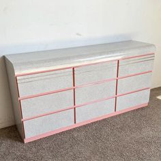 a white and pink dresser sitting on top of a carpeted floor next to a wall