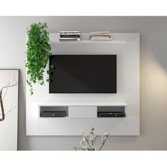 a tv mounted on the wall above a table with flowers and books in front of it