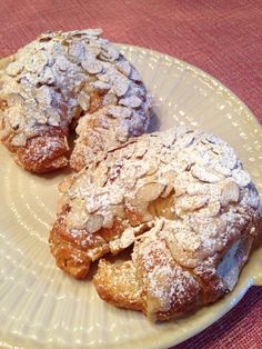 two croissants covered in powdered sugar sit on a plate with a red tablecloth