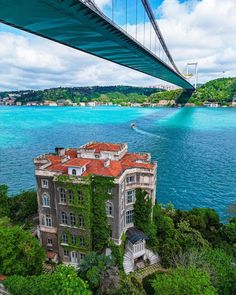 an old building with ivy growing on it and a suspension bridge in the background over blue water