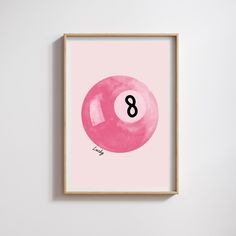 a pink ball with the number eight on it is hanging in a wooden frame against a white wall