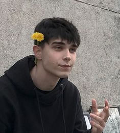 a young man with a flower in his hair sitting on a bench next to a wall