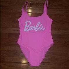 a pink bathing suit with the word barbie written in white on it, sitting on a wooden floor