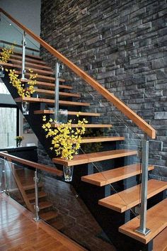 a wooden stair case with metal handrails next to a brick wall and flowers in a vase