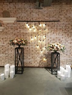 two vases with flowers and candles are on display in front of a brick wall