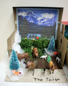 an open cardboard box with fake animals and trees in the inside, on top of a table