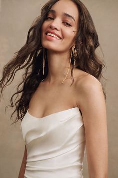 a woman in a white dress smiling and wearing gold earrings