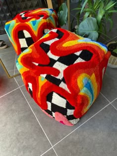 two colorful chairs sitting on top of a tile floor next to a potted plant