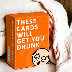 an orange box with the words these cards will get you drunk next to a pile of blankets