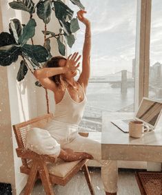 a woman sitting on a chair in front of a window with her arms raised up