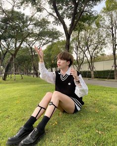 a person sitting in the grass with their legs crossed and one hand up to her chest