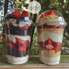 two desserts in plastic containers with strawberries and cream on top are sitting on a table