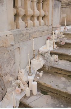 candles are lined up on the steps near flowers and vases in front of an old building