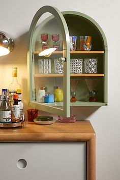 a shelf with glasses and bottles on it next to a wall mounted light that is turned on