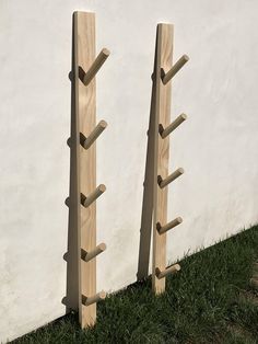 two wooden poles are in the grass near a white wall and one is leaning on it's side