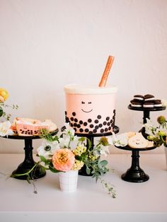 a table topped with cakes and cupcakes on top of black trays filled with flowers