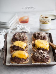 three hamburgers with cheese on them are sitting on a baking sheet and ready to be eaten