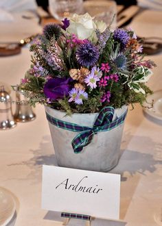 an arrangement of flowers in a bucket on a table with place cards and silverware